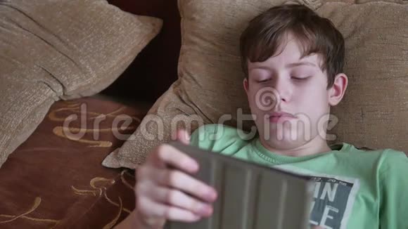 十几岁的男孩躺在室内的平板电脑社交媒体上少年男孩在床上的平板电脑上玩游戏视频的预览图