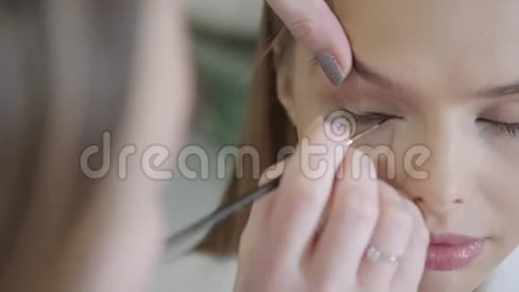 画眼睛化妆师为金发模特创造美丽的妆容美容和水疗中心概念视频的预览图