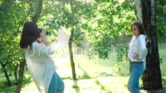 一位穿着白色衬衫的漂亮女孩职业摄影师正在一个柔和的背景下拍摄一个女孩在公园里的照片视频的预览图