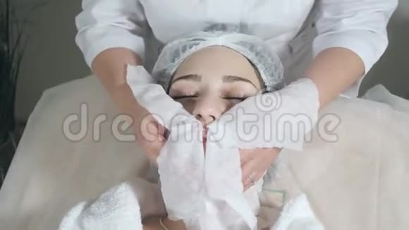 用无菌餐巾纸脸擦拭年轻漂亮的女人在美容院接受治疗面部清洁泡沫使用视频的预览图