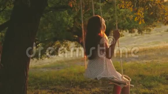 在公园日落时孩子们骑着绳子在橡树枝上摇摆特写镜头女孩笑高兴一个年轻女孩在视频的预览图