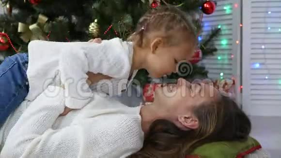 可爱的小女孩玩得开心在圣诞树旁边亲吻她的妈妈视频的预览图