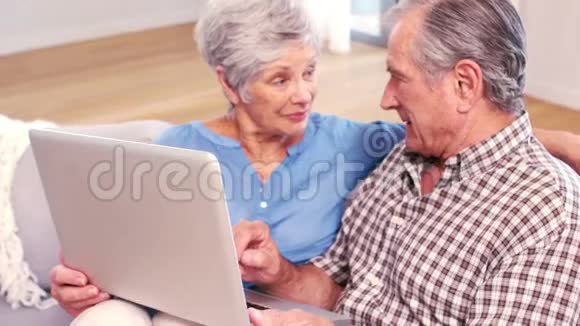 可爱的成熟夫妇在沙发上用笔记本电脑视频的预览图