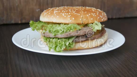 一个大的美味多汁的汉堡有三层切块新鲜生菜叶和奶酪放在一个时髦的白色盘子上视频的预览图