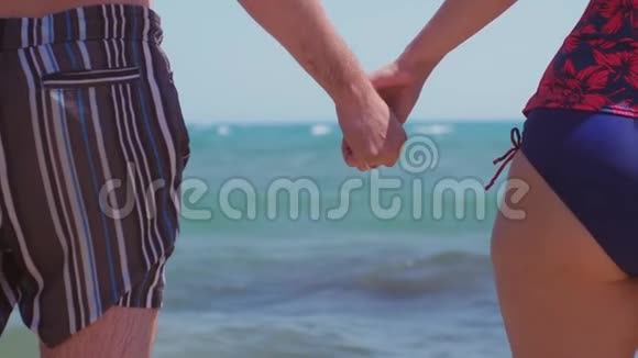 一对夫妇在海滩上的大海背景上牵手双手紧贴大海慢动作视频的预览图
