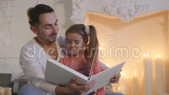 平安夜年轻的父亲和女儿坐在壁炉前讲故事视频的预览图