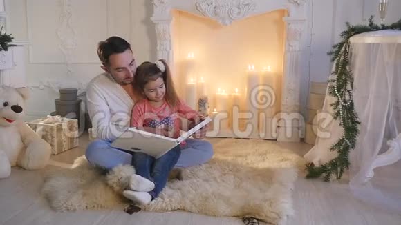 平安夜年轻的父亲和女儿坐在壁炉前讲故事视频的预览图