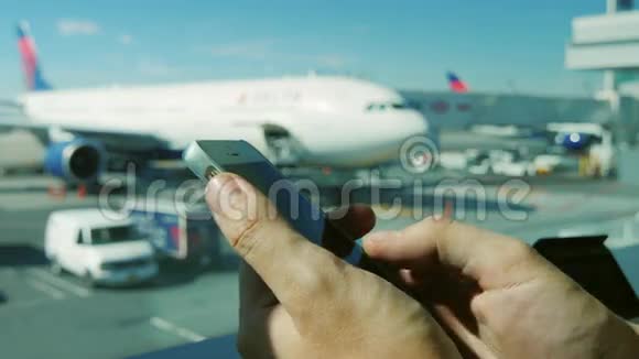 有智能手机的男人的手正在键入文本使用应用程序在机场窗户的背景下视频的预览图
