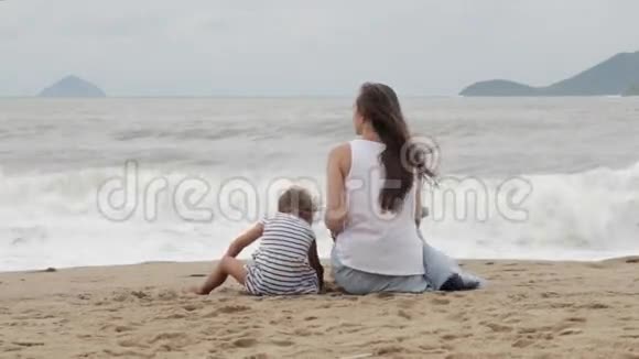 母亲带着女儿背对着镜头坐在沙滩上视频的预览图
