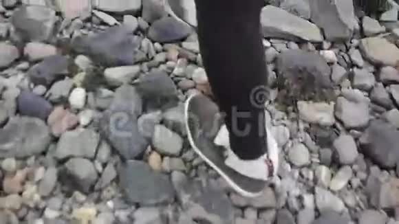 靠近一个女人带着棕色鞋子和黑色裤子走在海岸的石头上视频的预览图