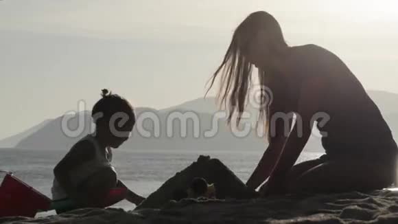 母亲和小女儿在海滩上建造沙堡的剪影视频的预览图