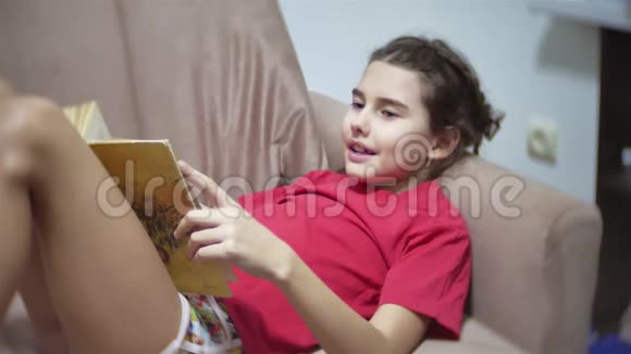 少女在室内沙发上看书躺在沙发上看一本室内书的女孩视频的预览图