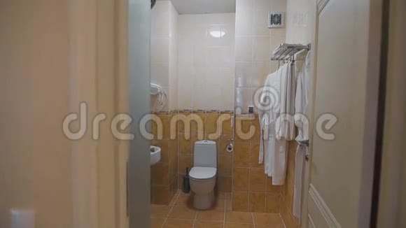 浴室有水槽厕所镜子和白色毛巾和浴袍挂在衣架上有房间的房间视频的预览图