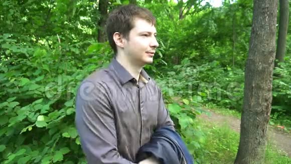 一个年轻人站在树林里把夹克扔在肩上慢动作视频的预览图