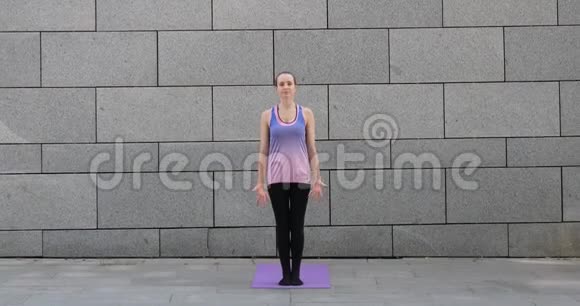 在城市的灰色城市背景下女人在粉色垫子上练习瑜伽健身运动视频的预览图