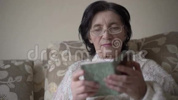 戴眼镜的老妇人在沙发上看祈祷书视频的预览图