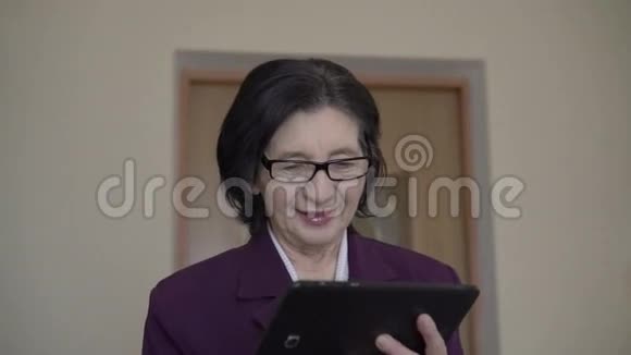 优雅的老商务女士站在墙上使用平板电脑视频的预览图