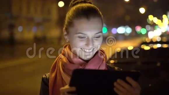 快乐的女孩微笑在街上的夜晚使用平板电脑4K视频的预览图