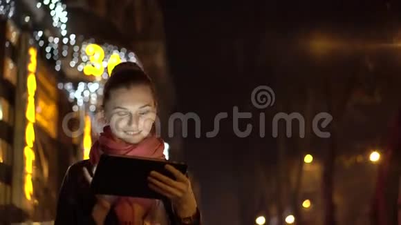 年轻的女孩晚上在明亮的街道上用平板电脑照明4K视频的预览图