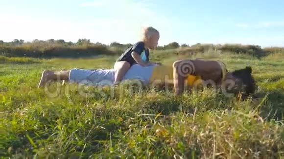 年轻强壮的父亲做俯卧撑他的小儿子在他的背上运动员在草地上做俯卧撑视频的预览图