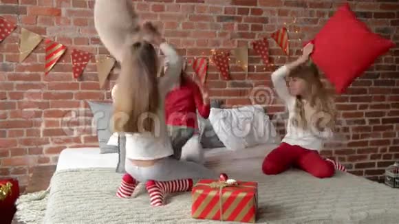 穿着睡衣的三胞姐妹用枕头安排了打斗卧室装饰着圣诞花环和圣诞节视频的预览图
