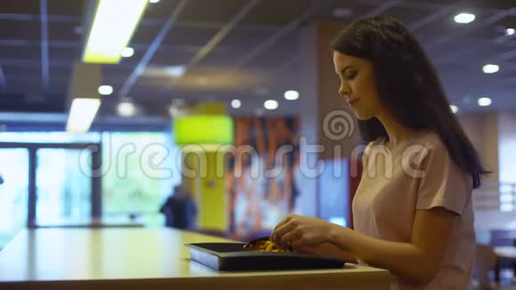 漂亮的女人在快餐店里吃脆炸薯条不健康的小吃视频的预览图
