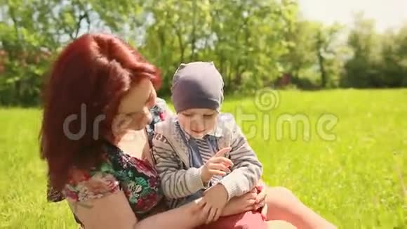 夏日里坐在草地上的母亲和儿子快乐的微笑视频的预览图