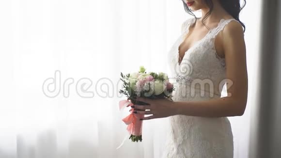 一位黑发新娘站在窗前嗅着新娘的花束视频的预览图