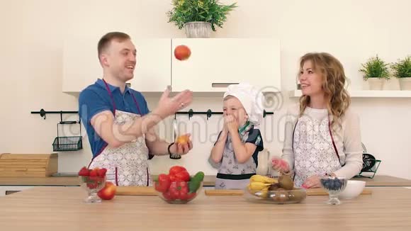 一家人正在厨房准备沙拉爸爸和妈妈把苹果扔起来儿子在笑视频的预览图