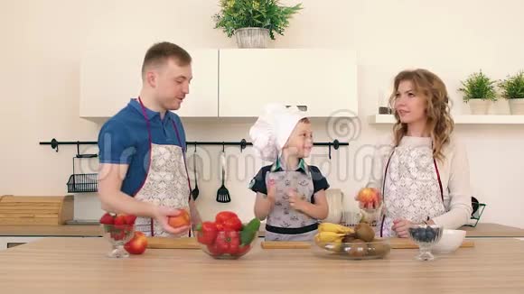 一家人正在厨房准备沙拉爸爸和妈妈把苹果扔起来儿子在笑视频的预览图