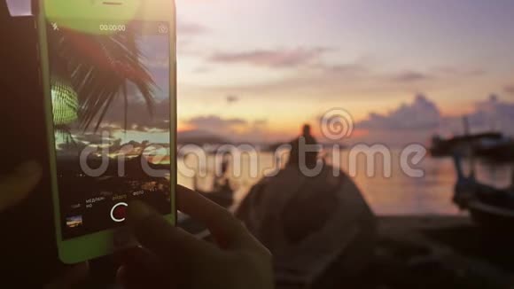 在海滩上坐着的时候女人用手机拍着日落的视频3840x21604k视频的预览图