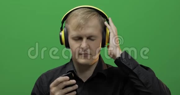 男人用无线黄色耳机听音乐跳舞绿色屏幕视频的预览图