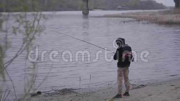 年轻自信的渔夫穿着卡其裤清晨在城市附近的河流里旋转钓鱼钓竿和一个视频的预览图
