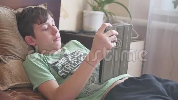 少年躺在平板社交媒体上男孩少年在床上的室内平板电脑上玩游戏视频的预览图