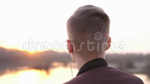 年轻英俊的男人在日落时在海滩上听音乐慢动作视频的预览图