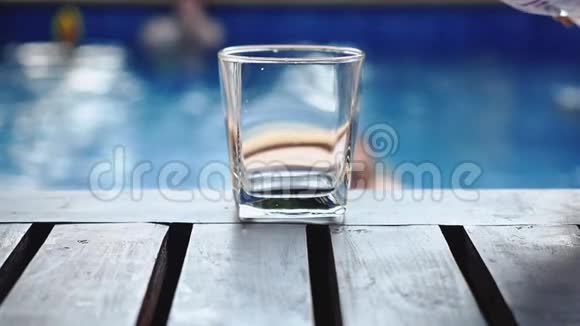 在游泳池附近的木桌上用玻璃杯倒淡水动作缓慢高清1920x1080视频的预览图