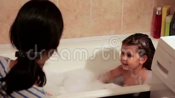 美丽的女孩沐浴在泡沫中吹泡沫她笑了和她妈妈玩得很开心玩玩具视频的预览图
