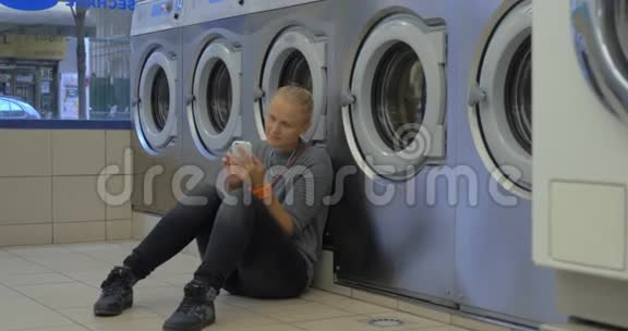在洗衣店里用智能手机的女人视频的预览图