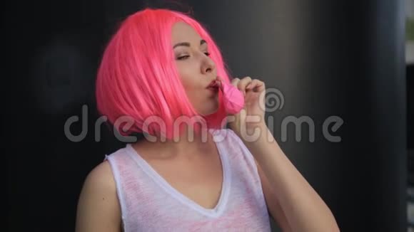 时尚时髦的时髦少女戴着粉色假发吹着红色气球的特写肖像视频的预览图