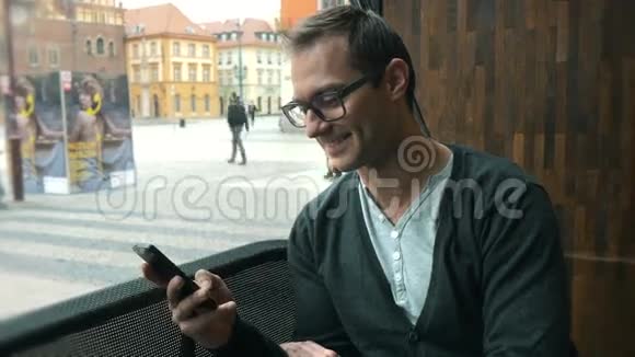 一个英俊的男人坐在城市的一家窗户咖啡馆旁用手机发短信视频的预览图