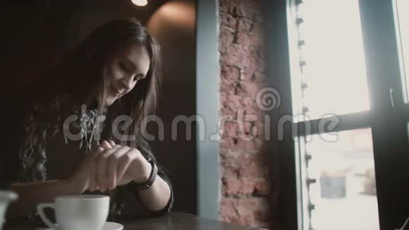 在loftcafe4k一个女人用她的智能手表触摸屏喝着咖啡看着窗外视频的预览图
