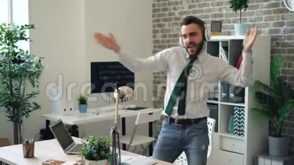 在现代办公室一个英俊的年轻人用耳机听音乐跳舞视频的预览图