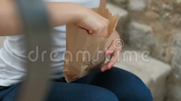 年轻的女人手里拿着新鲜的面包坐在外面的长凳上视频的预览图