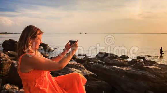 红岩金发女郎在日落时使用iPhone视频的预览图