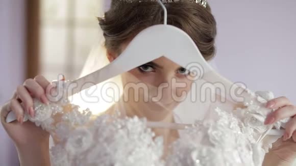 美丽可爱的新娘穿着睡衣拿着一件婚纱的衣架结婚的早晨漂亮又整洁的女人视频的预览图