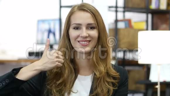年轻女孩在工作时竖起大拇指满意地坐在办公室里视频的预览图