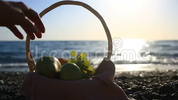 海滩上的水果篮手在海浪的背景下从葡萄串中取出葡萄视频的预览图