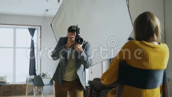 年轻漂亮的女模特在摄影棚里用数码相机拍照时为摄影师摆姿势视频的预览图