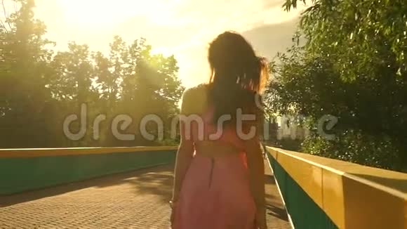 苗条的黑发女孩穿着粉红色的裙子在桥上散步慢动作安定夹视频的预览图