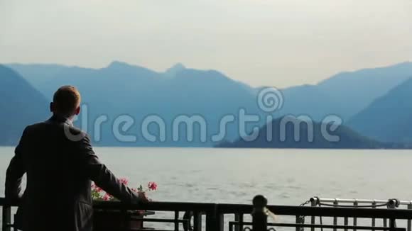 英俊的新郎在意大利科莫观看山和湖景的剪影背面视频的预览图